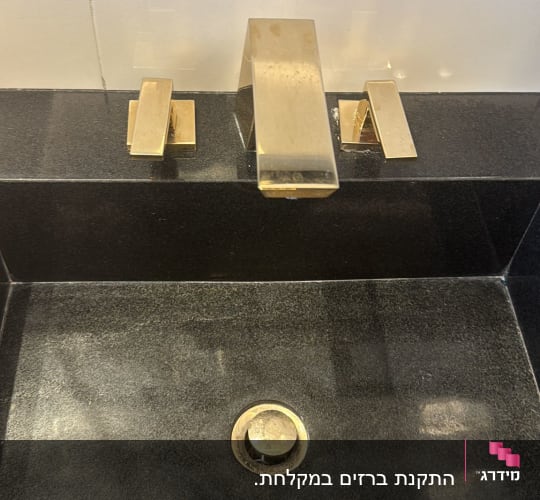 ברז כיור זהב עם ידיות על משטח שחור